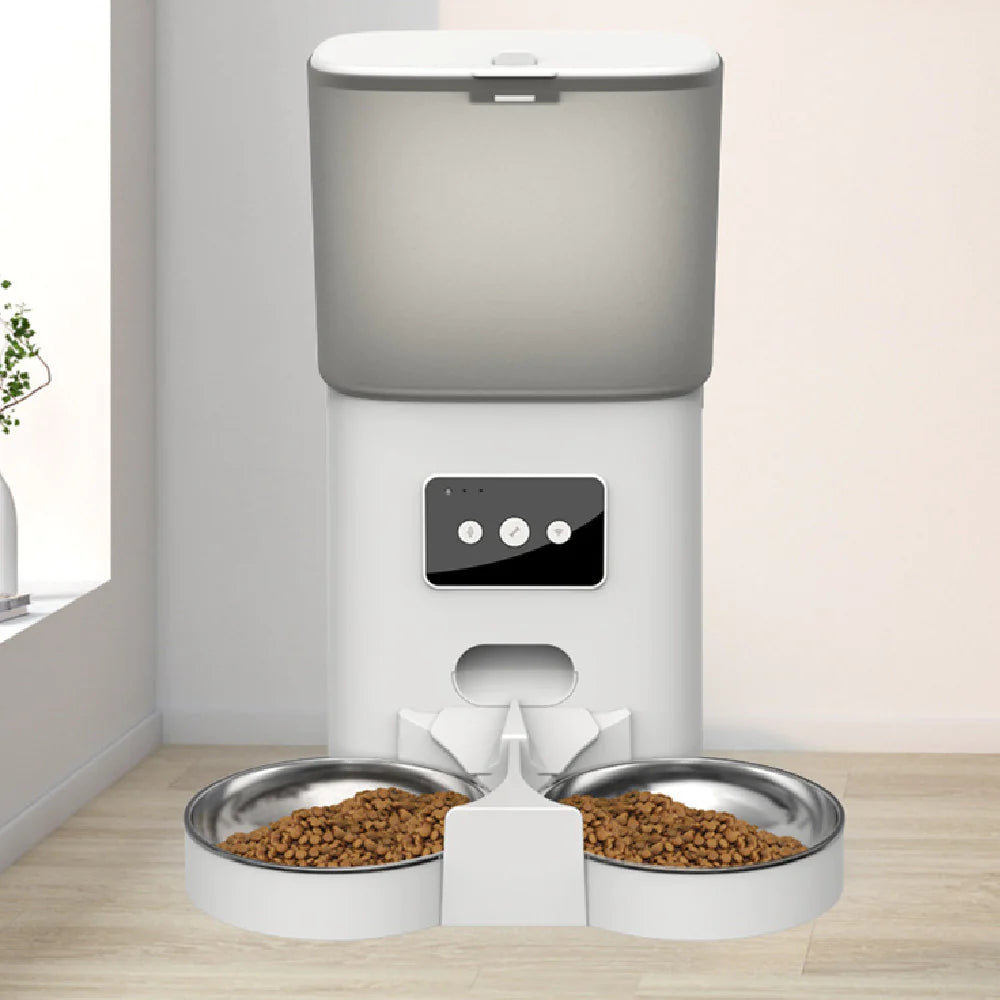 Automated pet feeder with two bowls of food on a wooden floor.